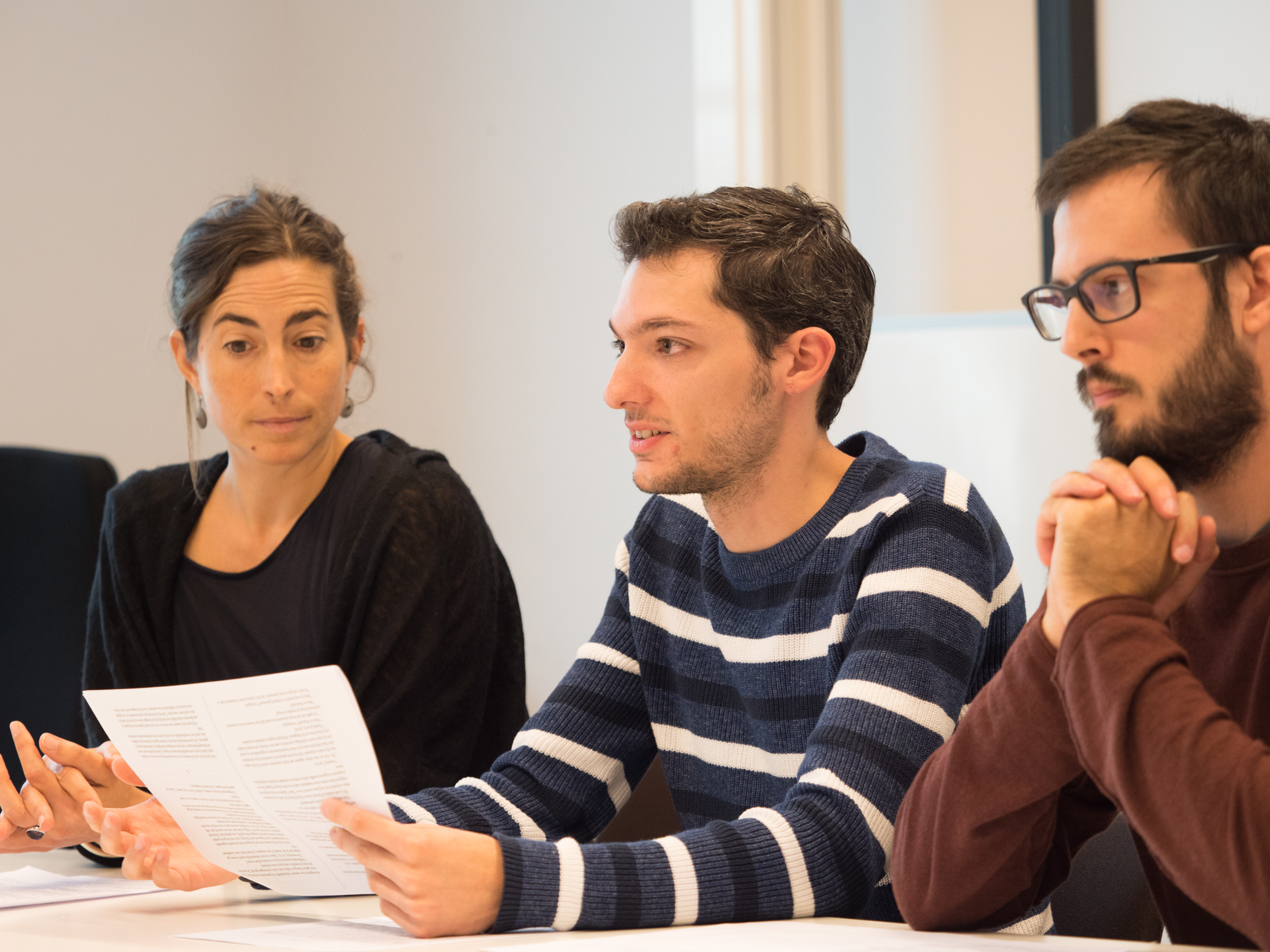 Drie deelnemers van een cursus naast elkaar. De middelste jongen leest iets voor van papier.