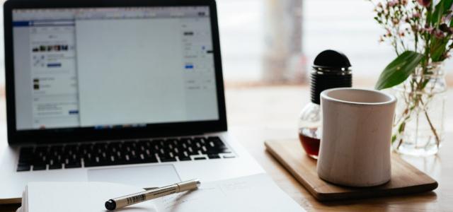 Foto van een tafel met laptop en mok koffie.